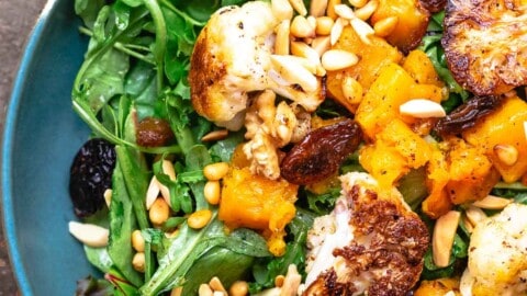 roasted cauliflower and butternut salad on a bed of greens, topped with nuts and raisins, on a blue plate