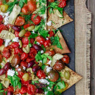 Mediterranean Roasted Tomato Nachos Recipe | The Mediterranean Dish. Homemade crispy nachos made with light, healthy flatbread. Loads of garlic roasted tomatoes and Mediterranean favorites on top! The perfect appetizer or little mezze dish!