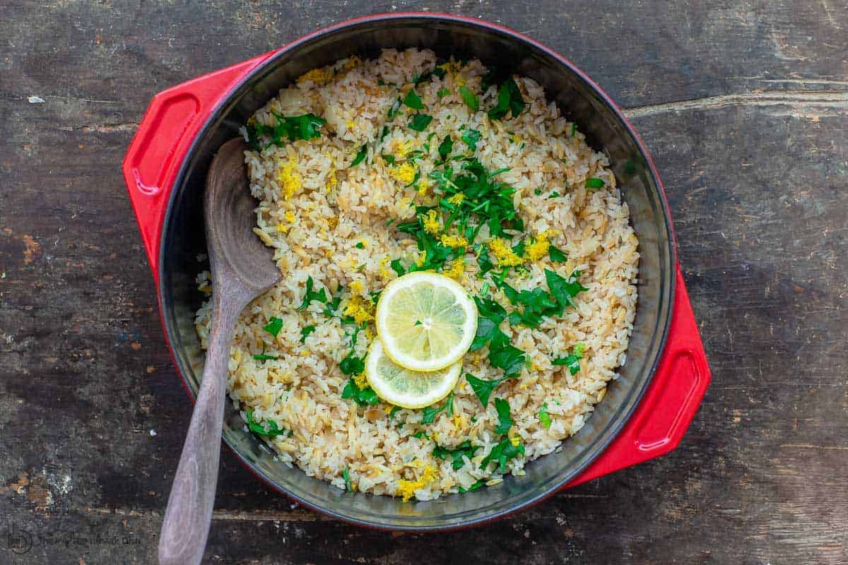 Greek lemon rice in pot cooking pot, garnished with fresh parsley, dill and lemon slices