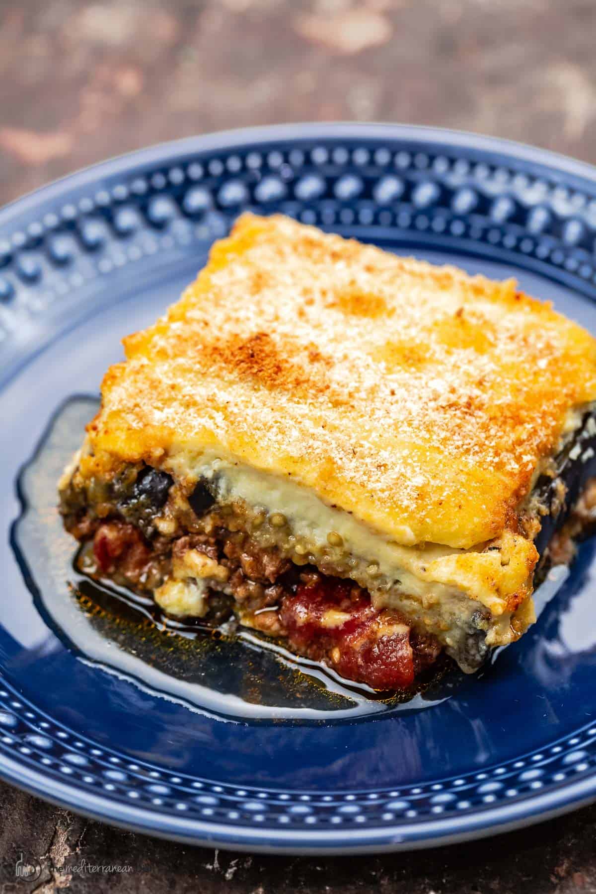 one slice of moussaka with eggplant, meat sauce, and bechamel on a blue plate
