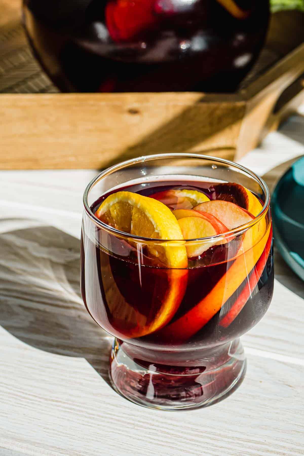 close up of a glass of red sangria with slices of oranges and apples.