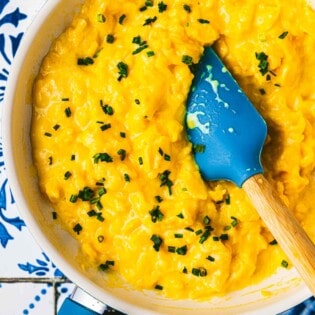 soft scrambled eggs topped with chives being stirred with a spatula in a saucepan.