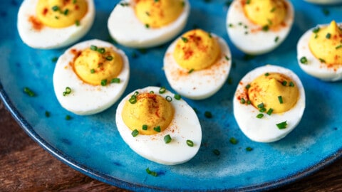 close up of 8 deviled eggs topped with paprika and chives on a plate .