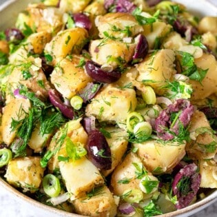 Close up of greek potato salad with olives, dill, parsley, and green onion.