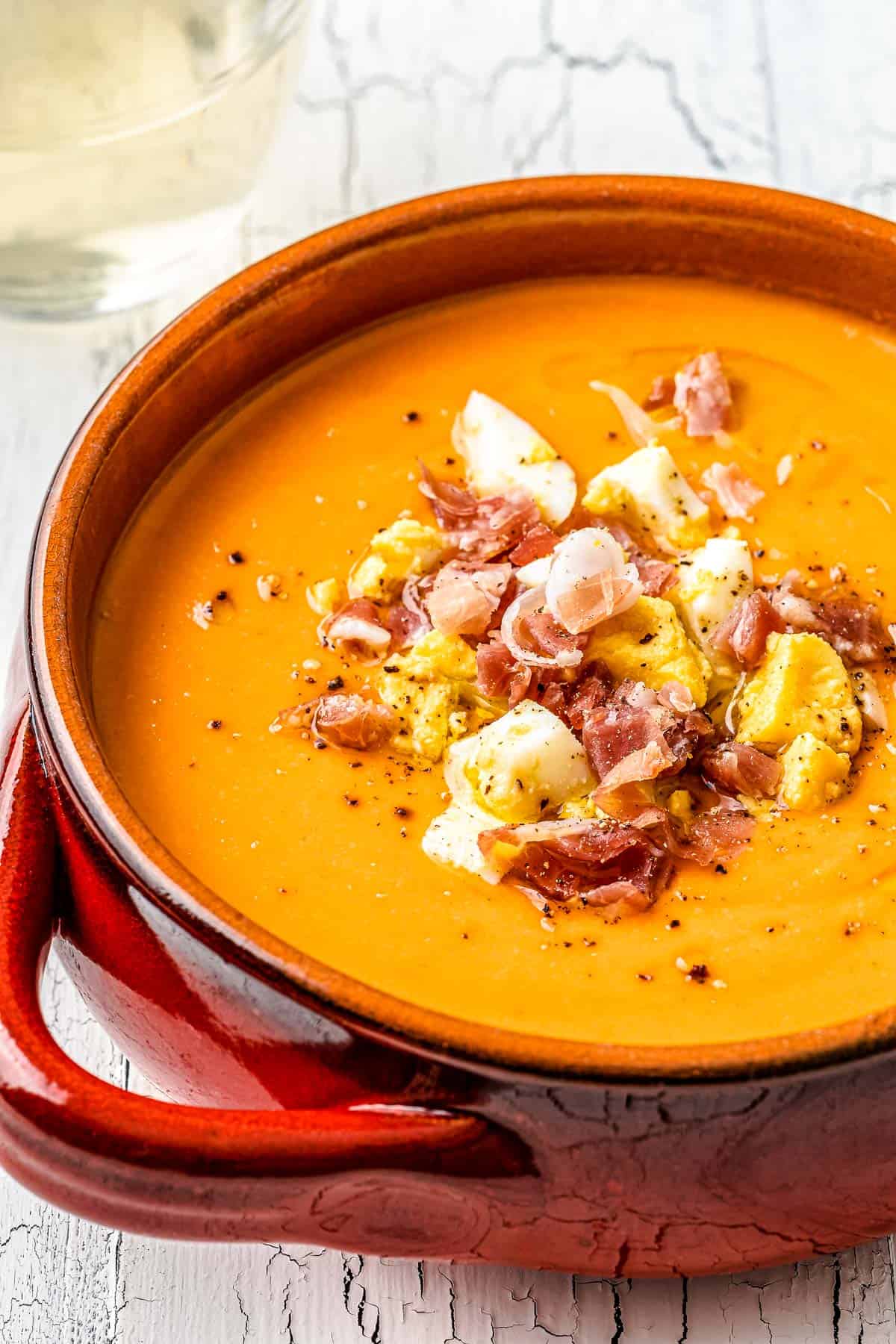 close up of a bowl of salmorejo spanish cold tomato soup topped with chopped hard boiled eggs and prosciutto.