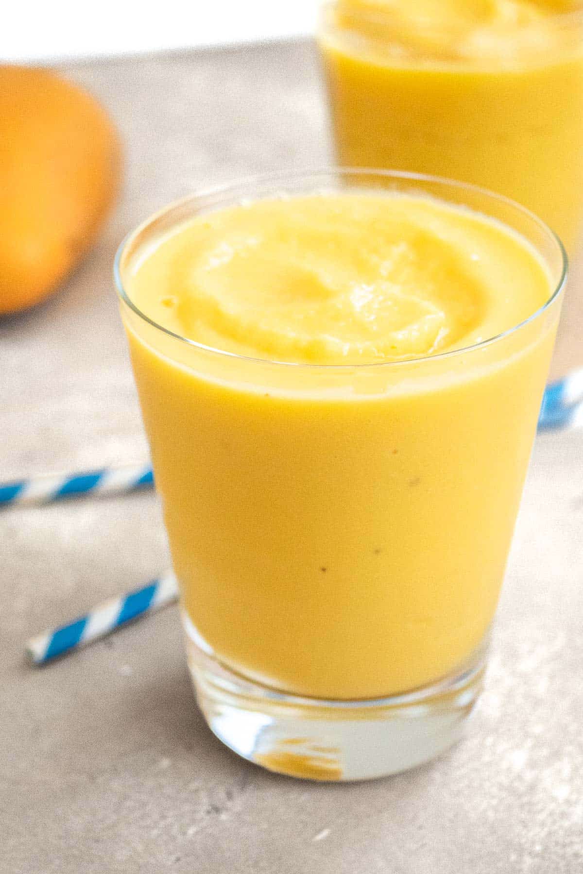 One mango smoothie in a glass with a straw on the side.