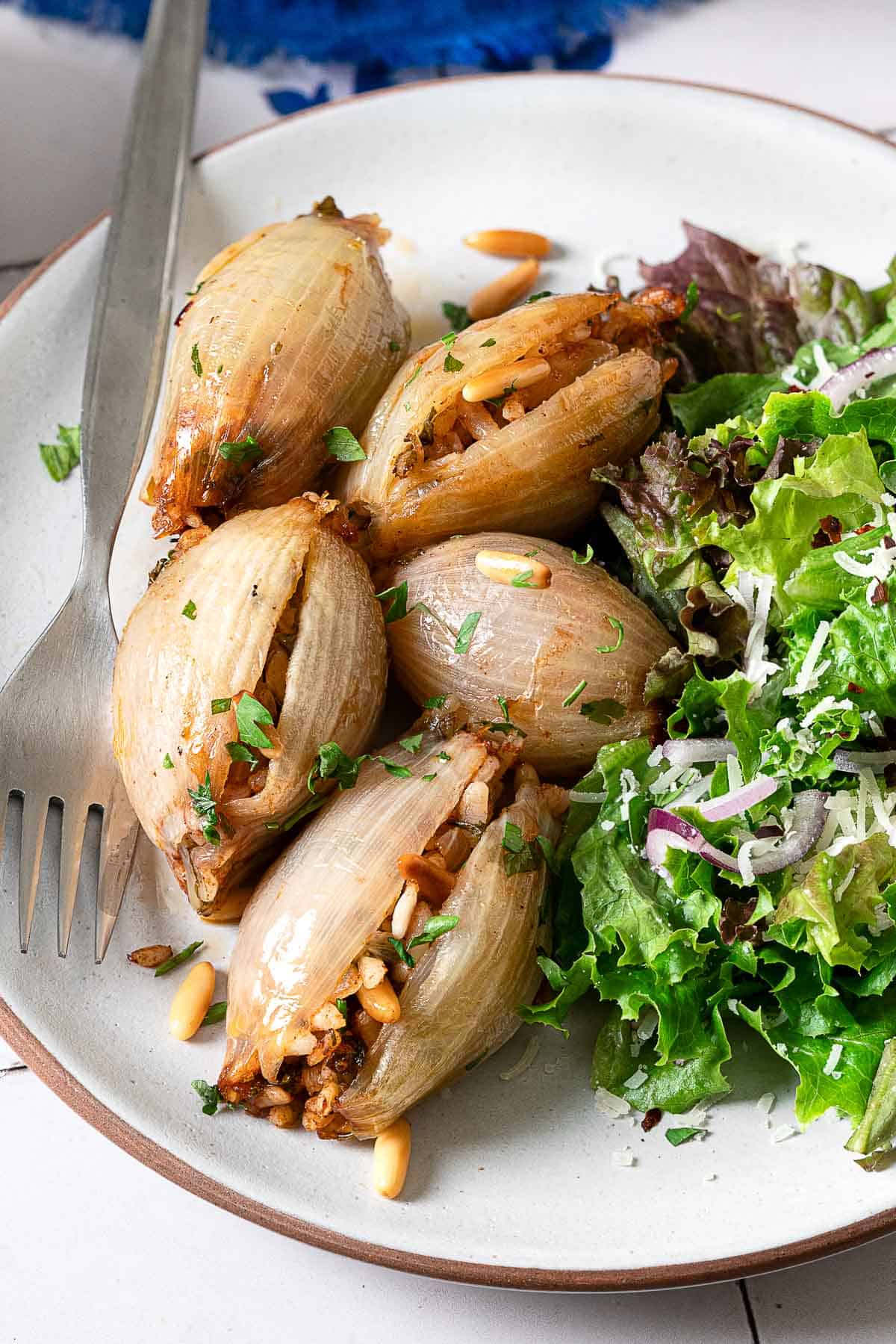 close up of stuffed onions on a plate with a side salad and a fork.