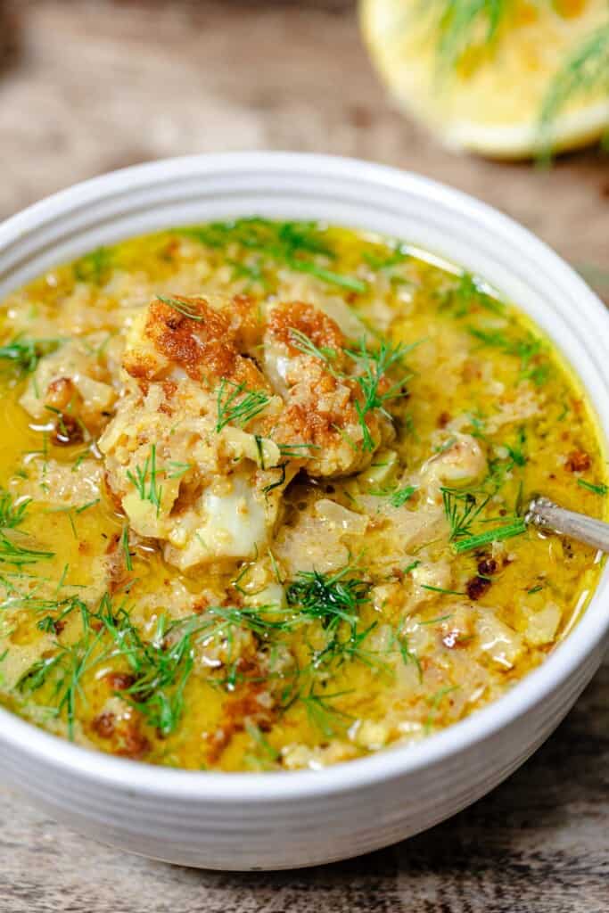 a close up of roasted cauliflower soup in a bowl with a spoon garnished with dill.