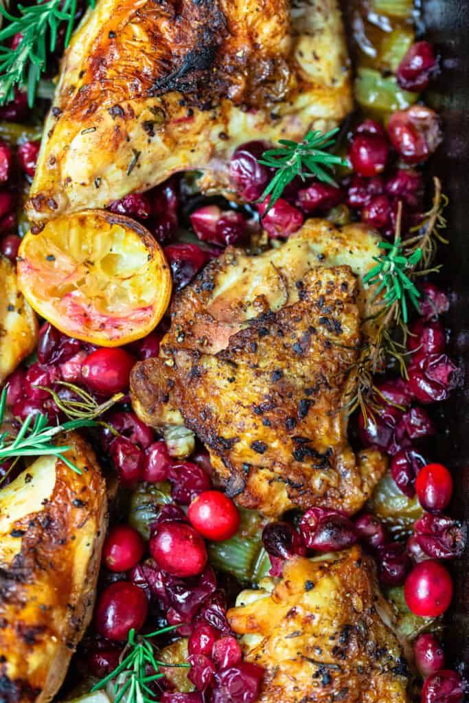 a close up of baked cranberry chicken topped with fresh cranberries, sprigs of fresh rosemary and lemon slices.