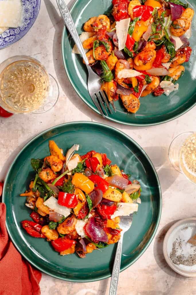 Sheet pan gnocchi with roasted bell pepper, red onion, cherry tomatoes, herbs, and parmesan shavings on a teal plate.