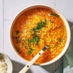 an overhead photo of a serving of pastina soup garnished with parsley and parmesan cheese in a bowl with a spoon.