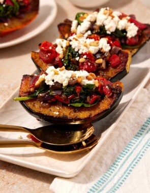 Three stuffed acorn squash quarters on a serving platter with large spoons.