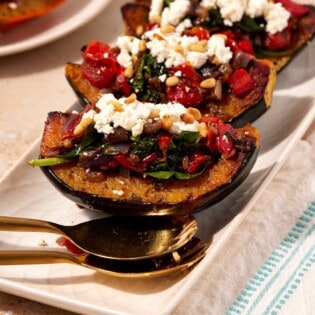 Three stuffed acorn squash quarters on a serving platter with large spoons.