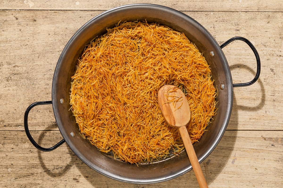 Fideos being toasted in a skillet with a wooden spoon.