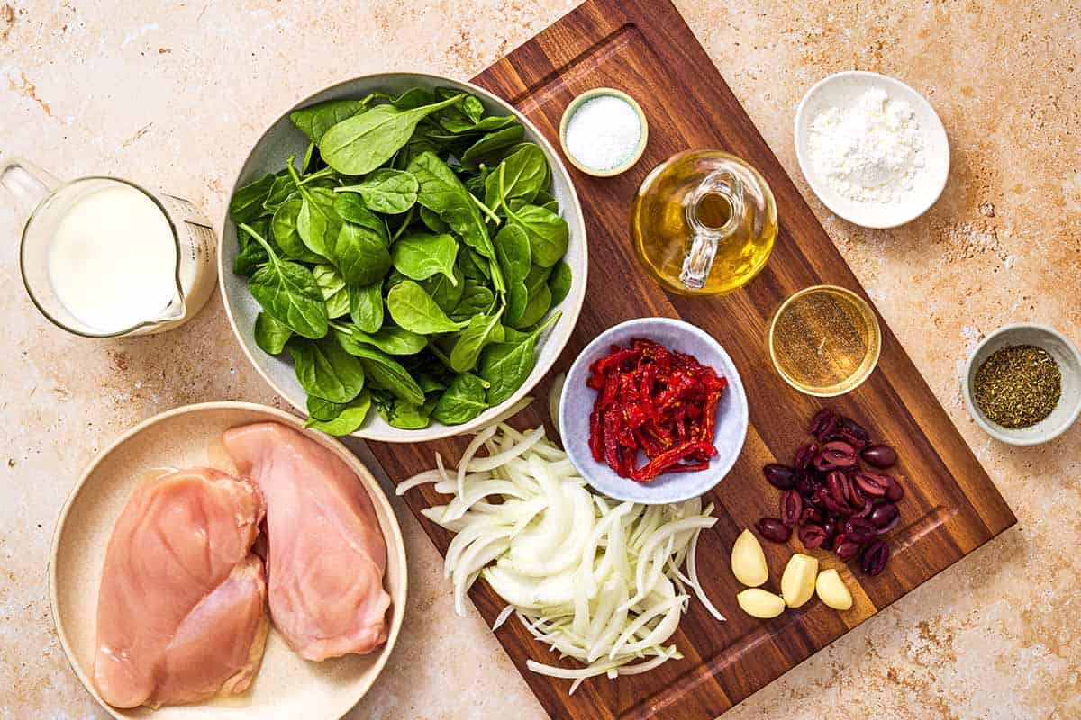 Ingredients for Sun Dried Tomato Chicken including chicken breasts, Italian seasoning, salt, olive oil, sun dried tomatoes, onion, garlic, white wine, whole milk, cornstarch, baby spinach, and kalamata olives.