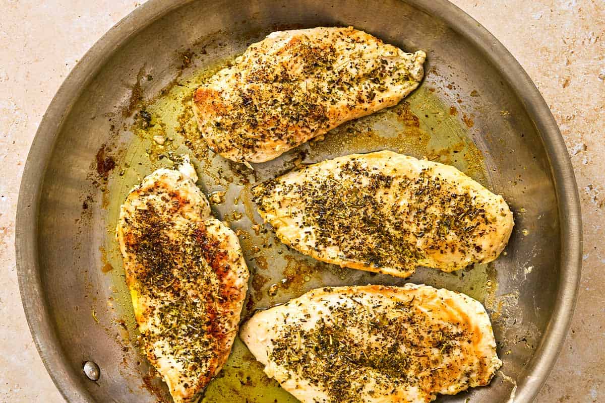 Seasoned chicken breast cutlets browning in a skillet with olive oil.
