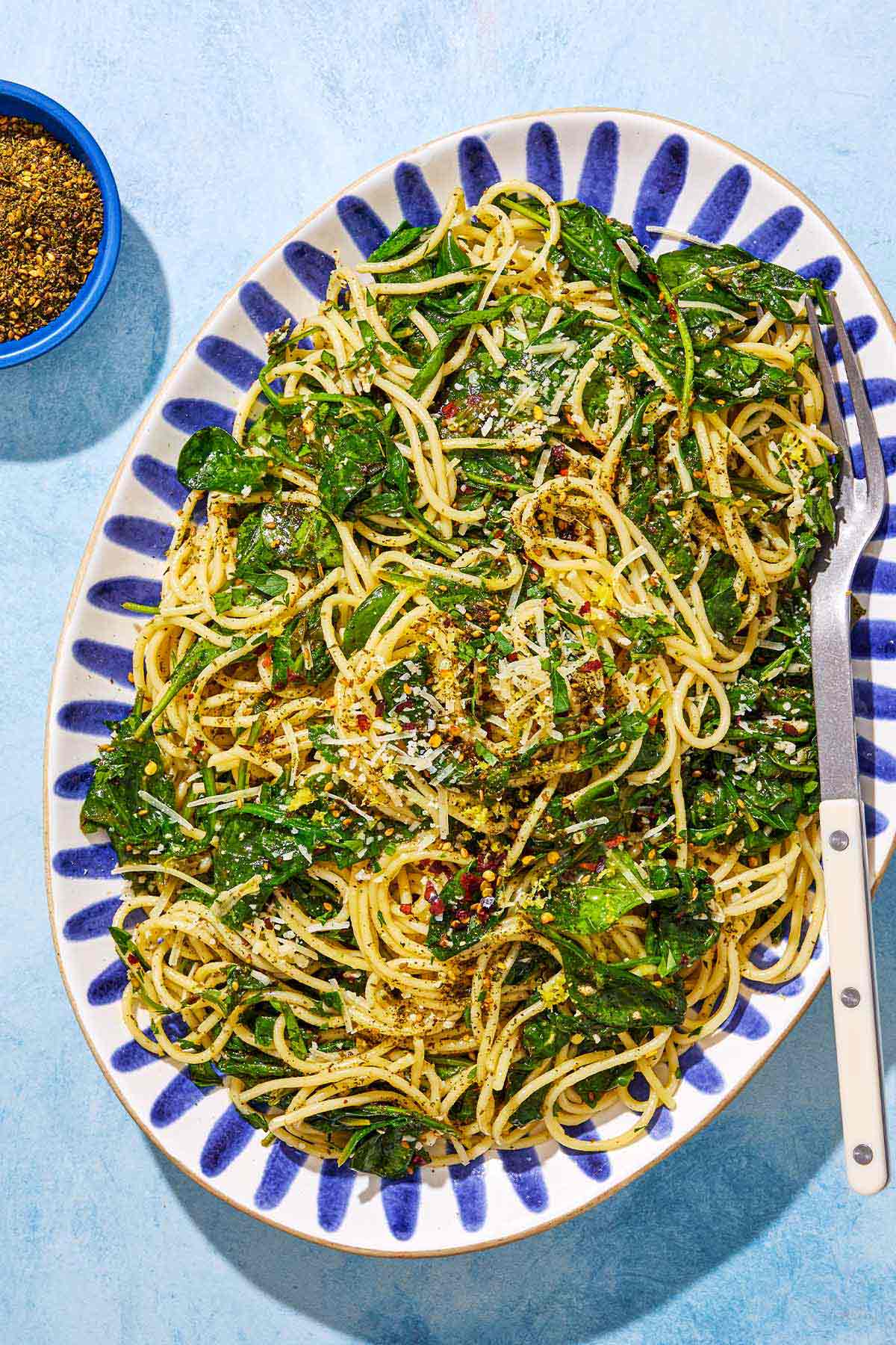 An overhead photo of za'atar garlic spinach pasta on a serving platter with a fork next to a small bowl of za'atar.