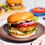 A close up of a chicken burger on plate next to a kitchen towel.