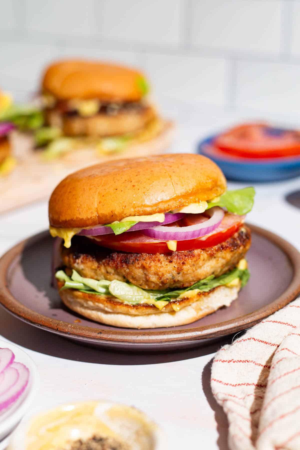 A close up of a chicken burger on plate next to a kitchen towel.