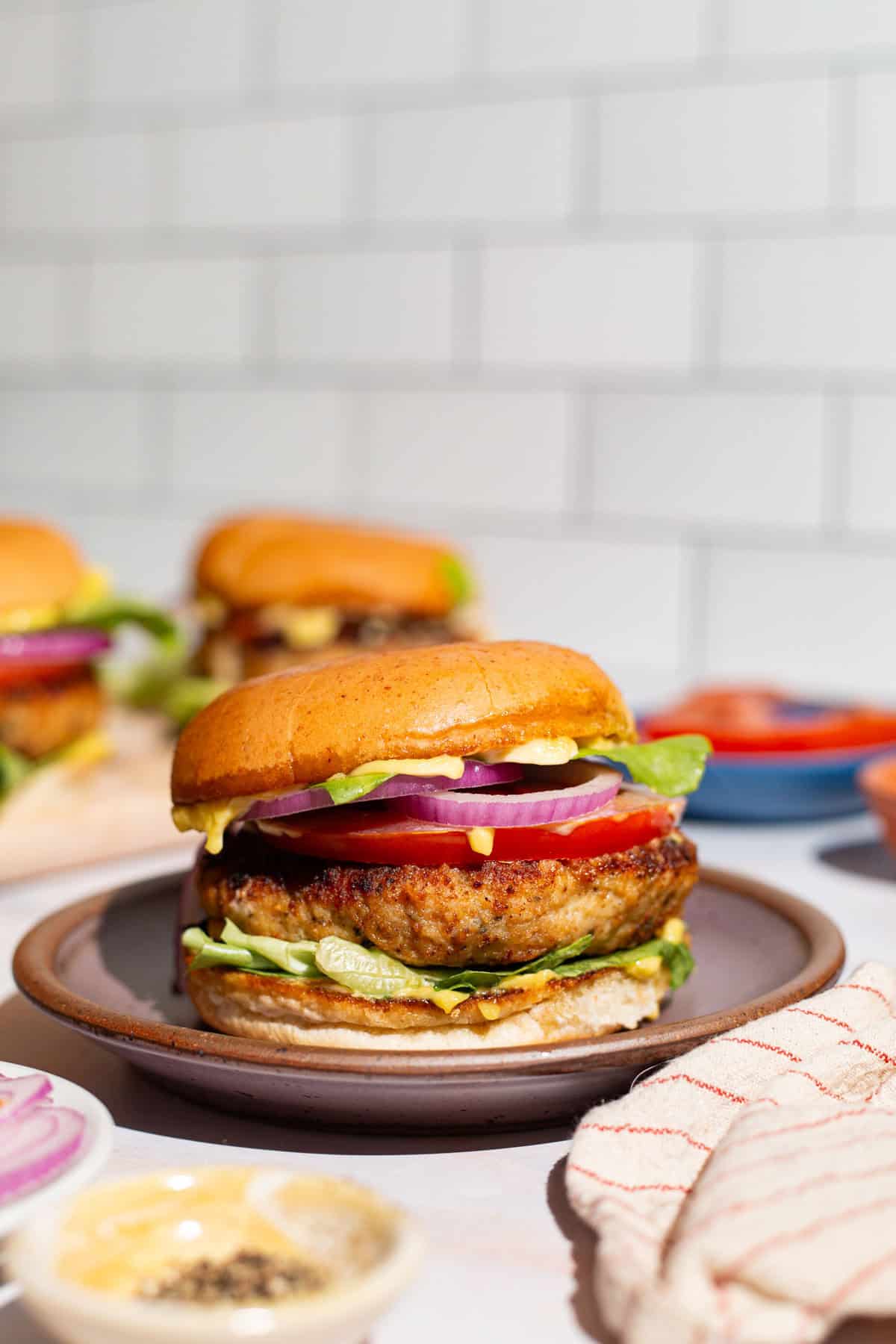 A close up of a chicken burger on plate next to a kitchen towel.