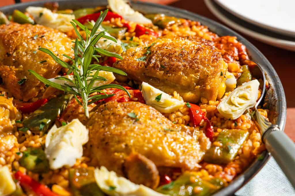 A close up of chicken paella in a large paella pan with a serving spoon.