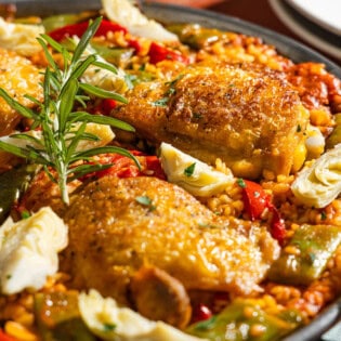 A close up of chicken paella in a large paella pan with a serving spoon.