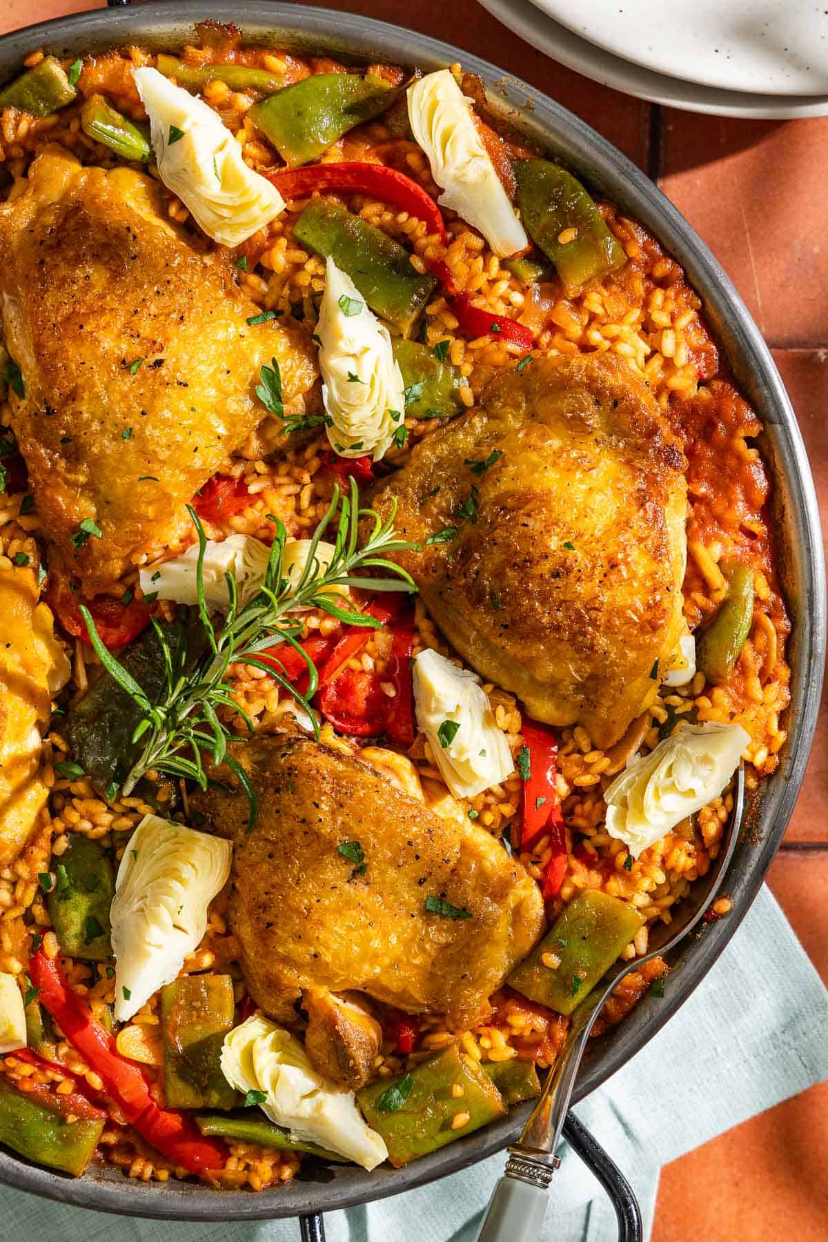 An overhead close up photo of chicken paella in a large paella pan with a serving spoon.