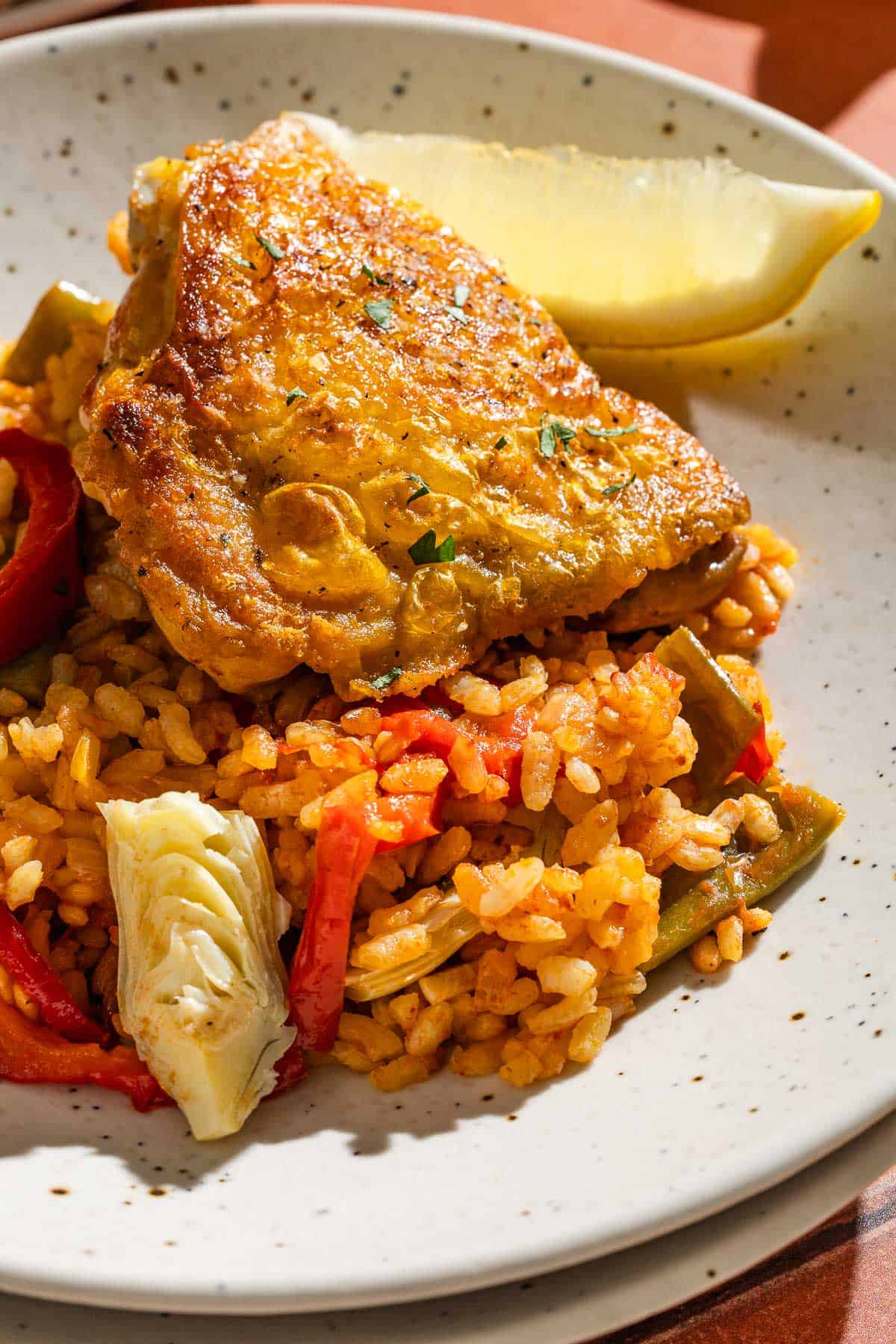 A close up of chicken paella on a plate with a lemon wedge.
