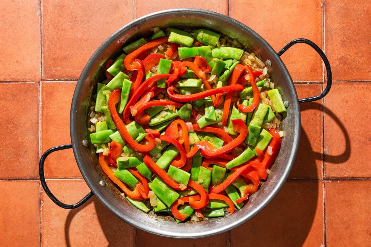 An overhead photo of the paella in a large paella pan just after the vegetable were added, before they were mixed with the other ingredients.