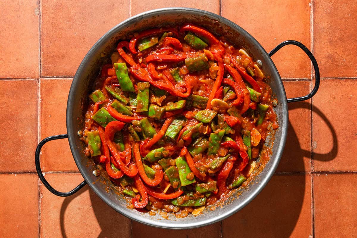 An overhead photo of the paella in a large paella pan after the vegetables were added and mixed with the rest of the ingredients.