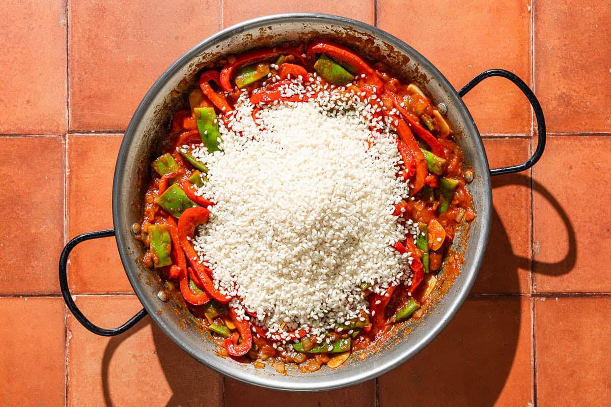 An overhead photo of the paella in a large paella pan just after the rice was added, before being mixed together.