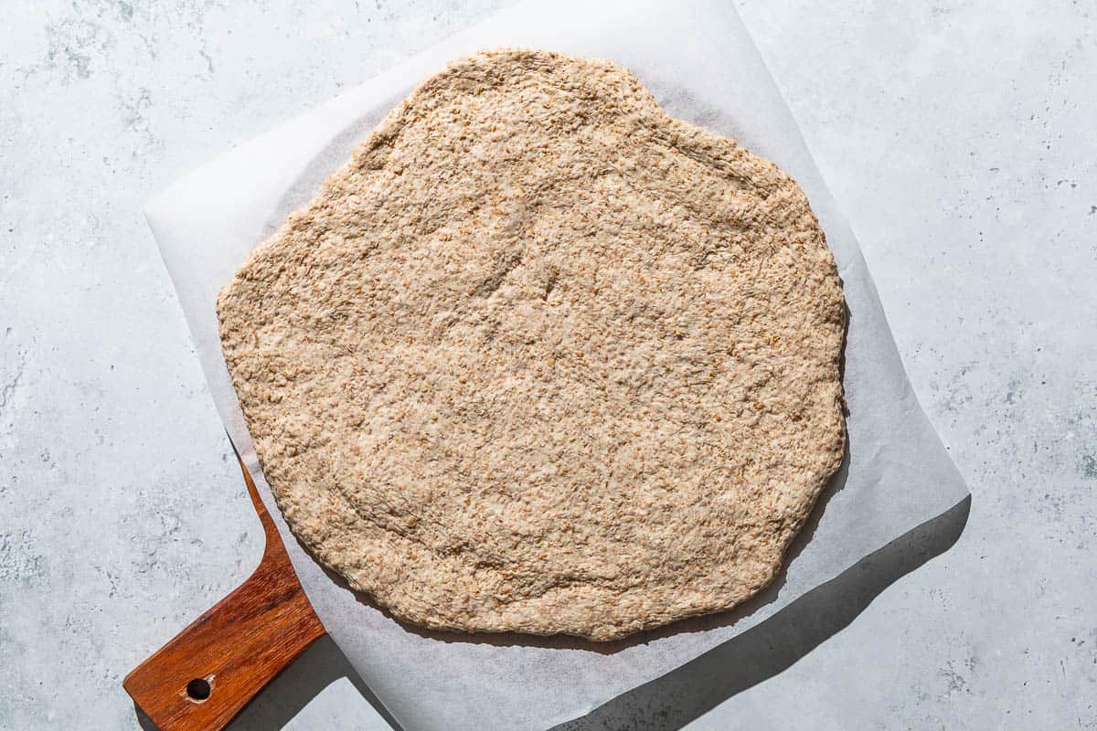 Unbaked pizza dough spread on a parchment lined wooden serving tray.