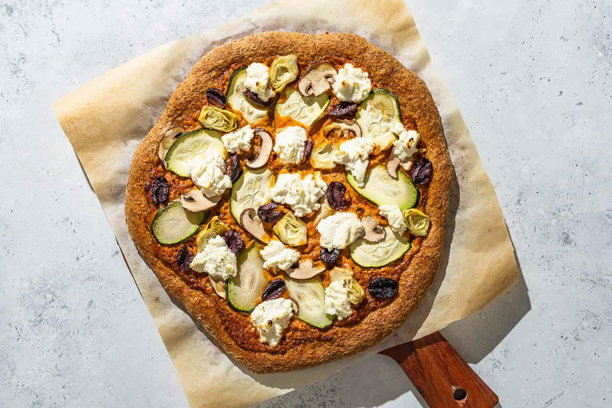 A baked vegetarian pizza on a parchment lined wooden serving tray.