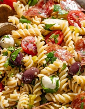 Close up side shot of Italian pasta salad in a serving bowl with two wooden serving spoons.