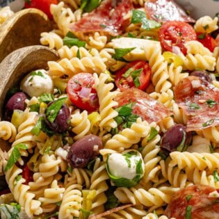 Close up side shot of Italian pasta salad in a serving bowl with two wooden serving spoons.