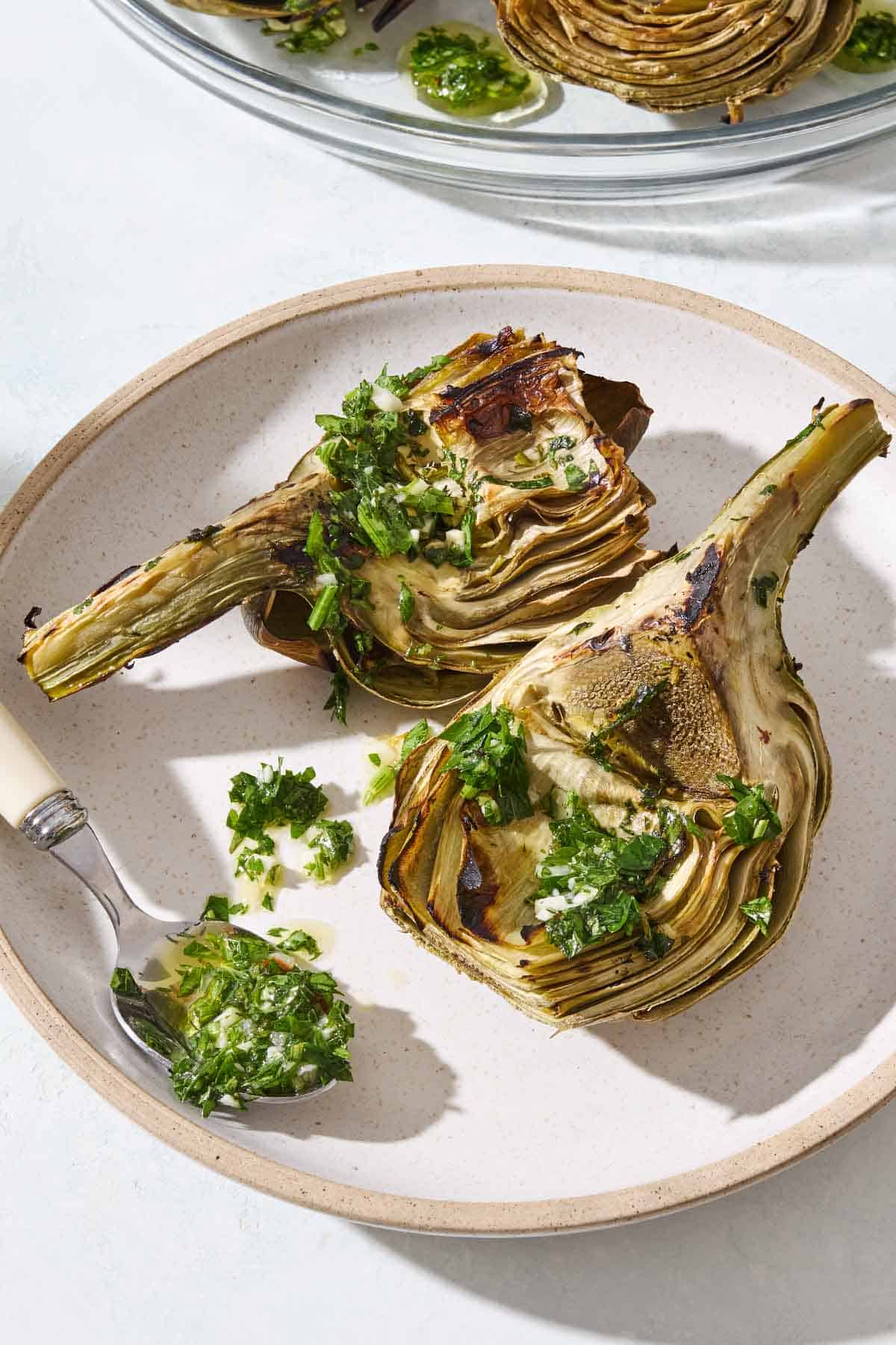 Two grilled artichoke quarters drizzled with marinade on a plate with a spoon.