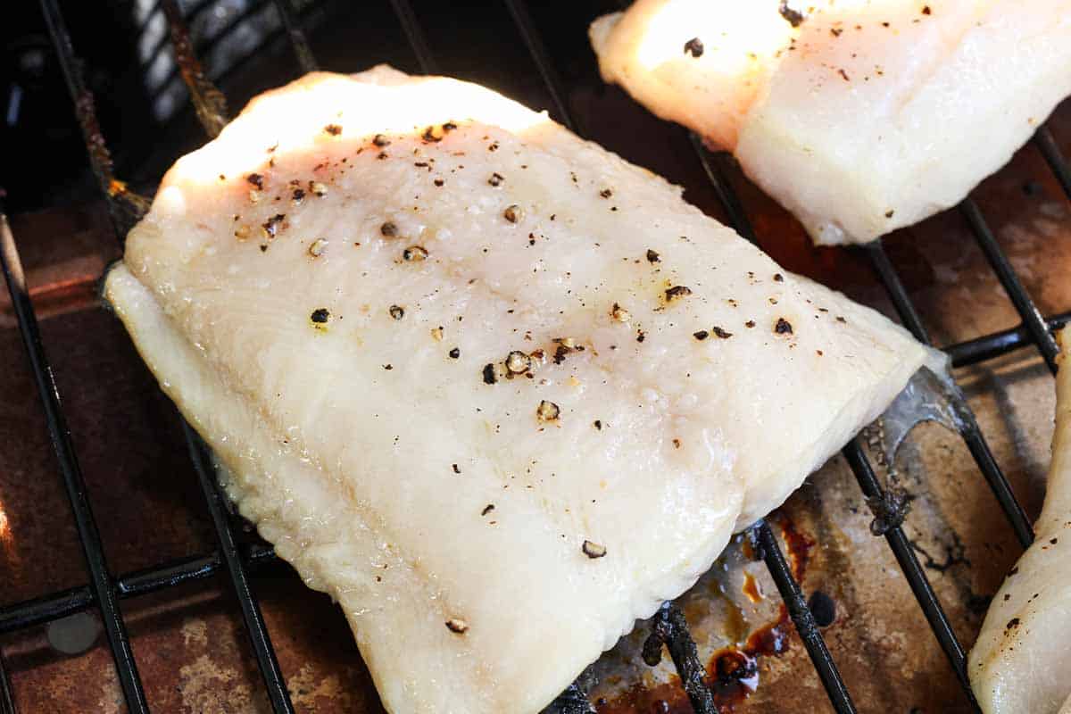 A close up photo of a cod filet seasoned with salt and pepper on a grill.