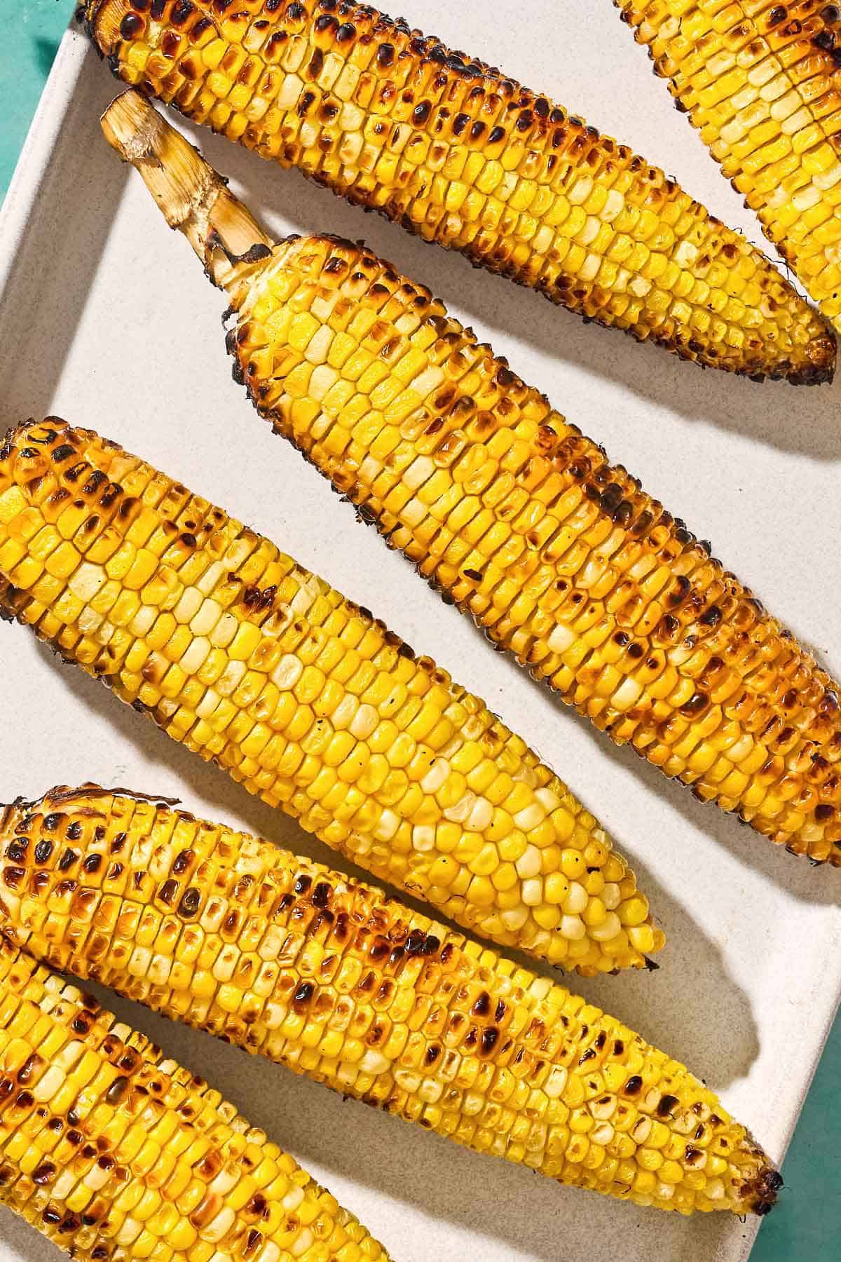 An overhead close up photo of 6 grilled corn on the cobs on a serving platter.