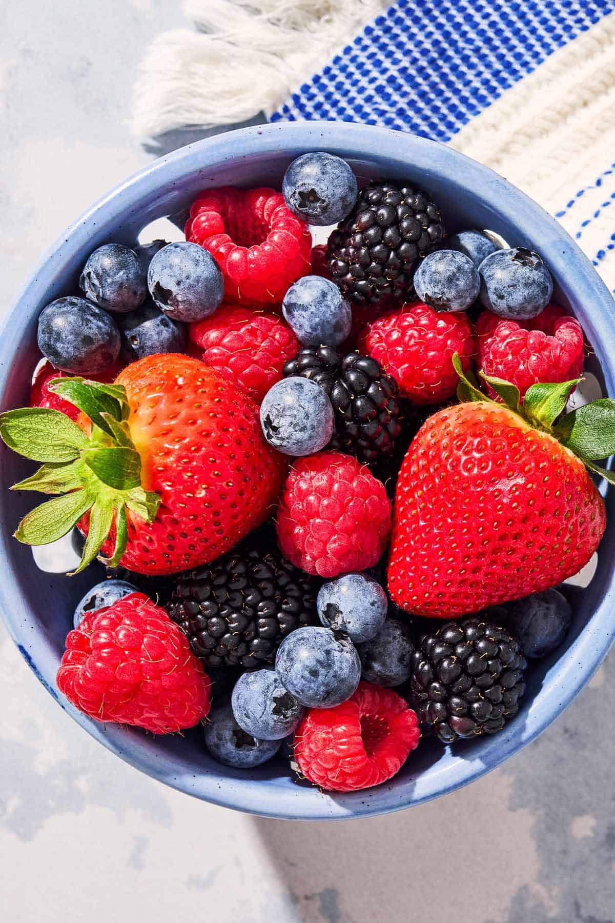 A close up of a blueberries, blackberries and strawberries in a bowl next to a kitchen towel
