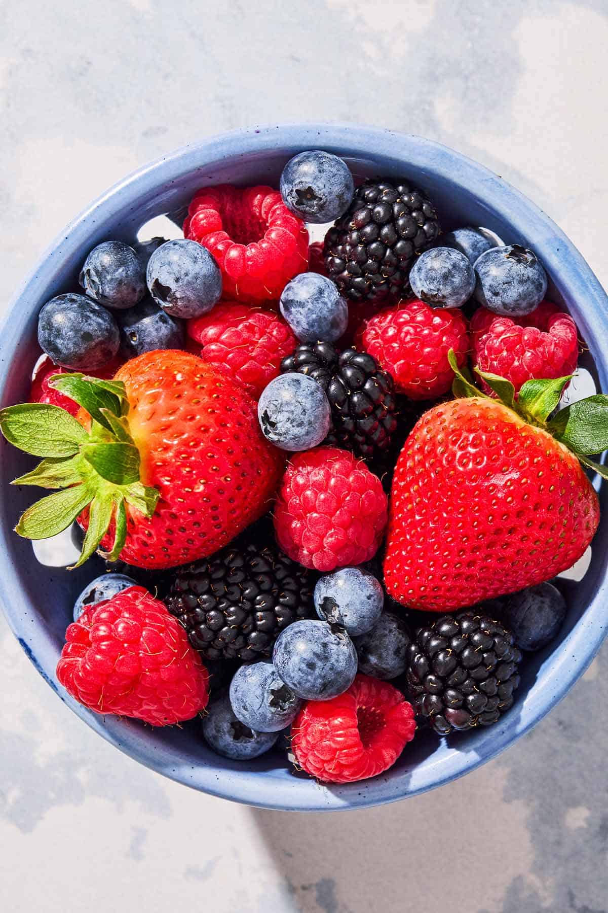 A close up of a blueberries, blackberries and strawberries in a bowl.