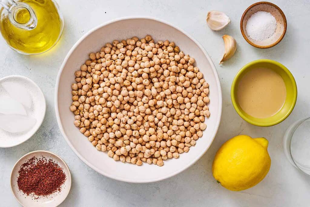 Ingredients for hummus including chickpeas, garlic, tahini paste, salt, lemon, water, ice cubes, olive oils and sumac.