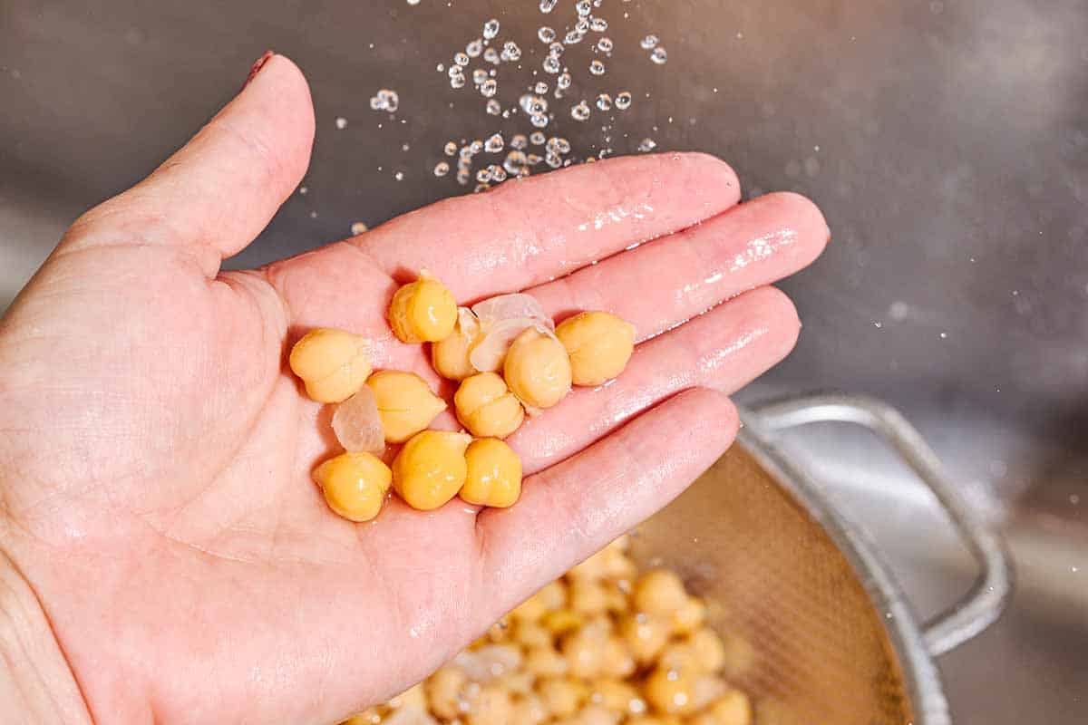 A hand holding some cooked chickpeas above a colander with the rest of the chickpeas.