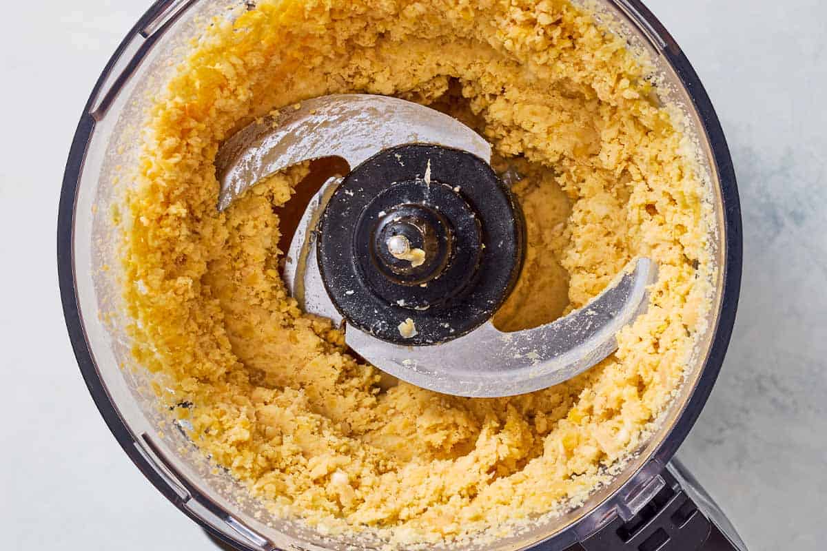 Pureed chickpeas and garlic in the bowl of a food processor fitted with a blade.