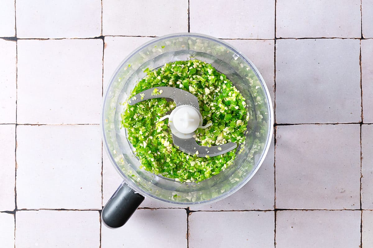 The chopped jalapeno and garlic in the bowl of a food processor fitted with a blade.