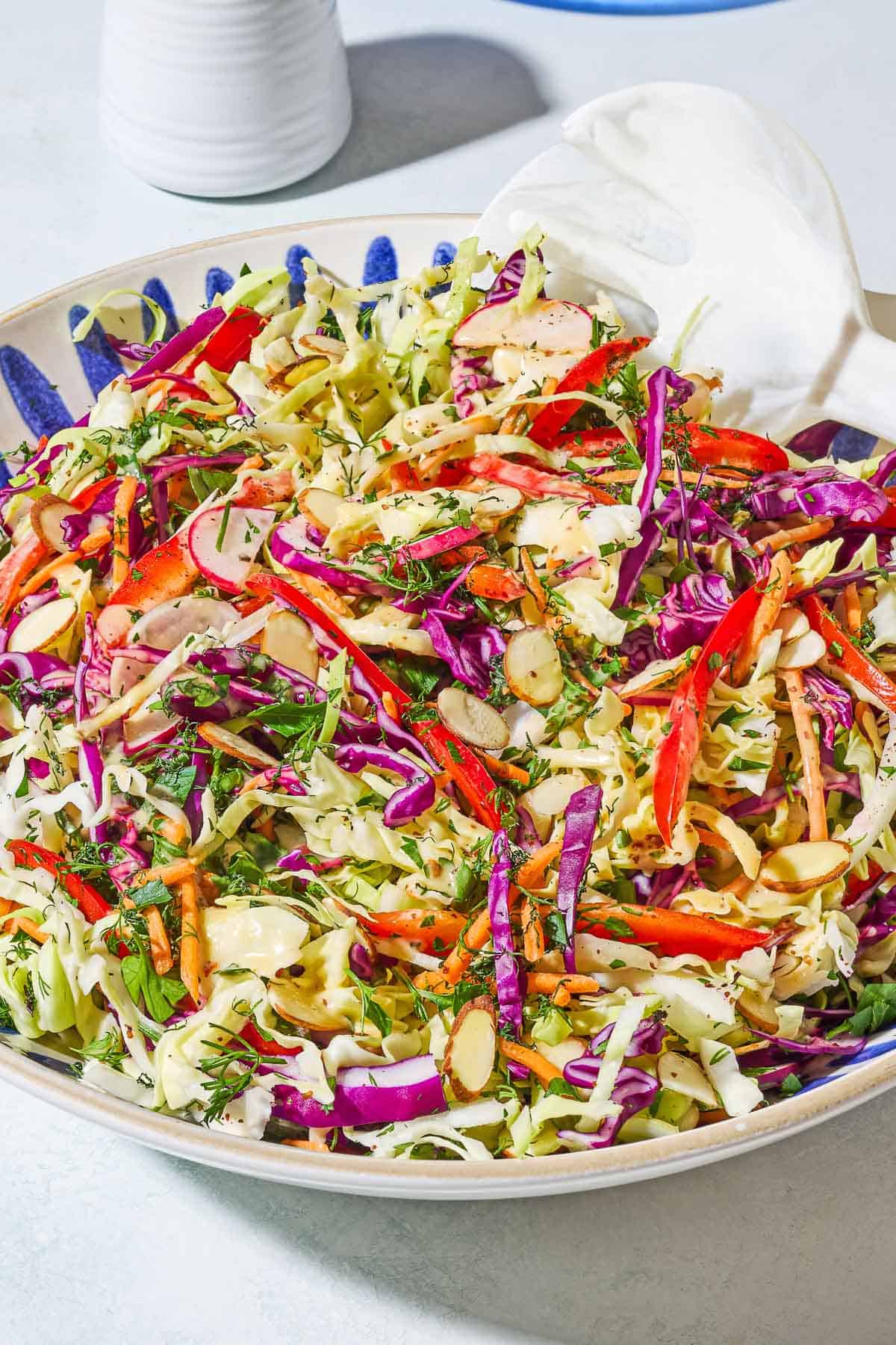 A close up of cabbage salad in a serving bowl with serving utensils.