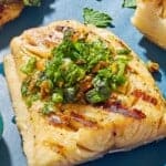 A close up of a grilled cod filet topped with a pistachio-herb salsa.