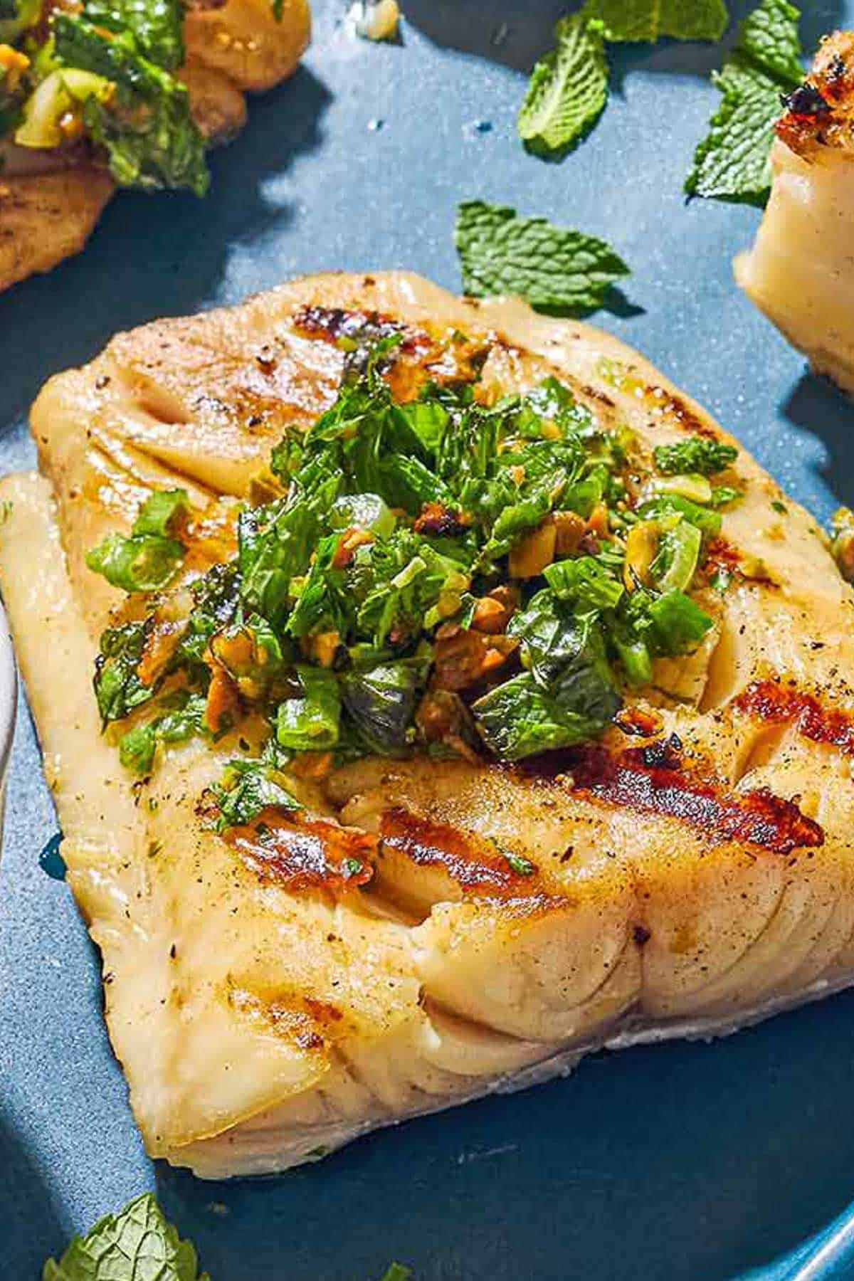 A close up of a grilled cod filet topped with pistachio-herb salsa.