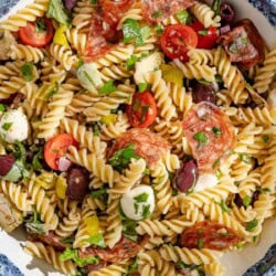 Overhead shot of Italian pasta salad in a serving bowl, showing the mozzarella, tomatoes, pepperoncini, fresh herbs, olives, salami, and artichoke hearts.
