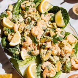 Three quarter short of shrimp salad on a romaine-lined serving platter with lemon wedges on the side.