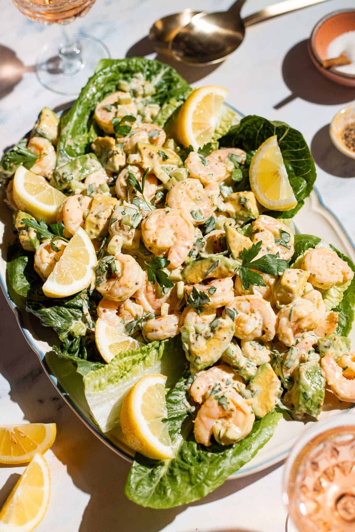 Three quarter short of shrimp salad on a romaine-lined serving platter with lemon wedges on the side.